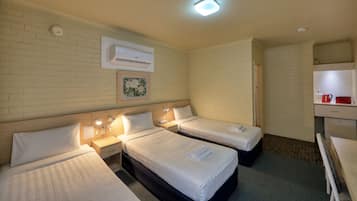 A hotel room with two single beds, a small desk, a chair, a nightstand, an air conditioning unit, and a painting on the wall.