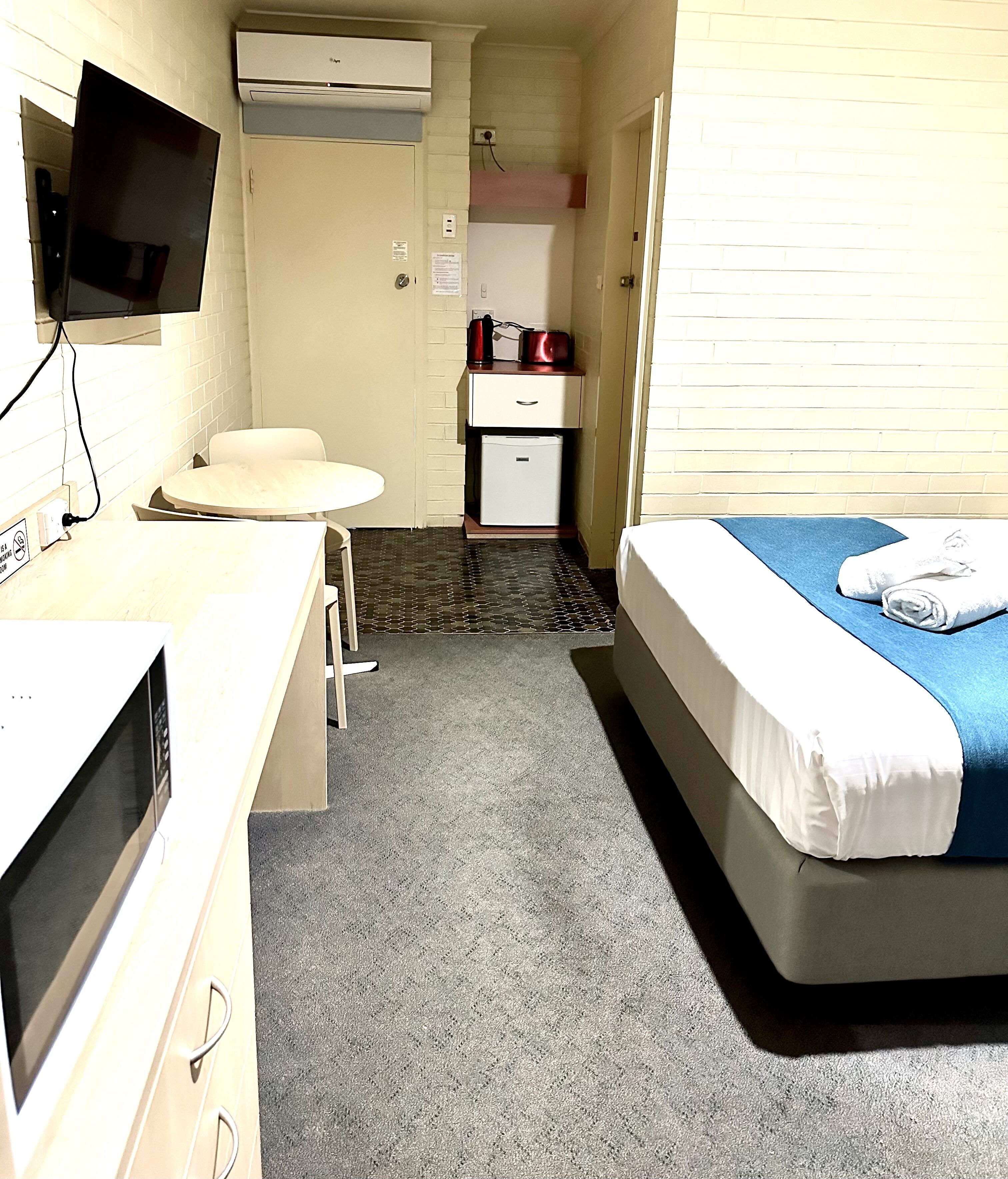Ein Hotelzimmer mit Bett, Schreibtisch mit Computer, kleinem Kühlschrank, Mikrowelle und Fernseher.