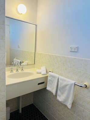 A bathroom with a large mirror above a sink, two faucets, and a towel rack with two towels.