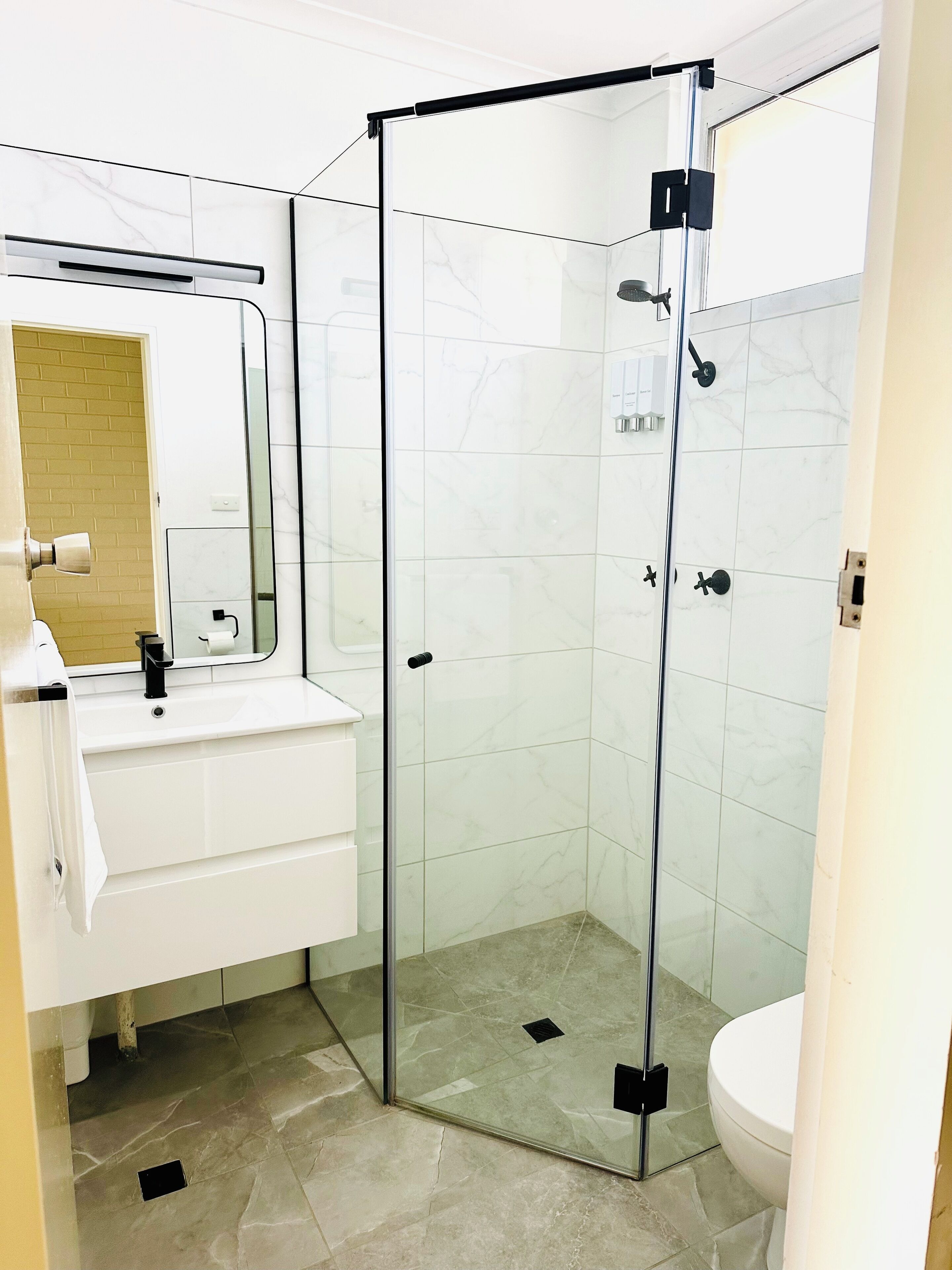 A modern bathroom with a glass-enclosed shower, a white sink, and a mirror above it.