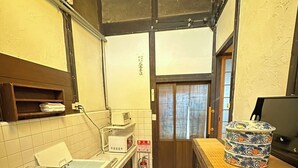 A narrow commercial kitchen with a microwave, a fire extinguisher, and a wooden counter with a decorative vase. - Korakuan (Kyoto)