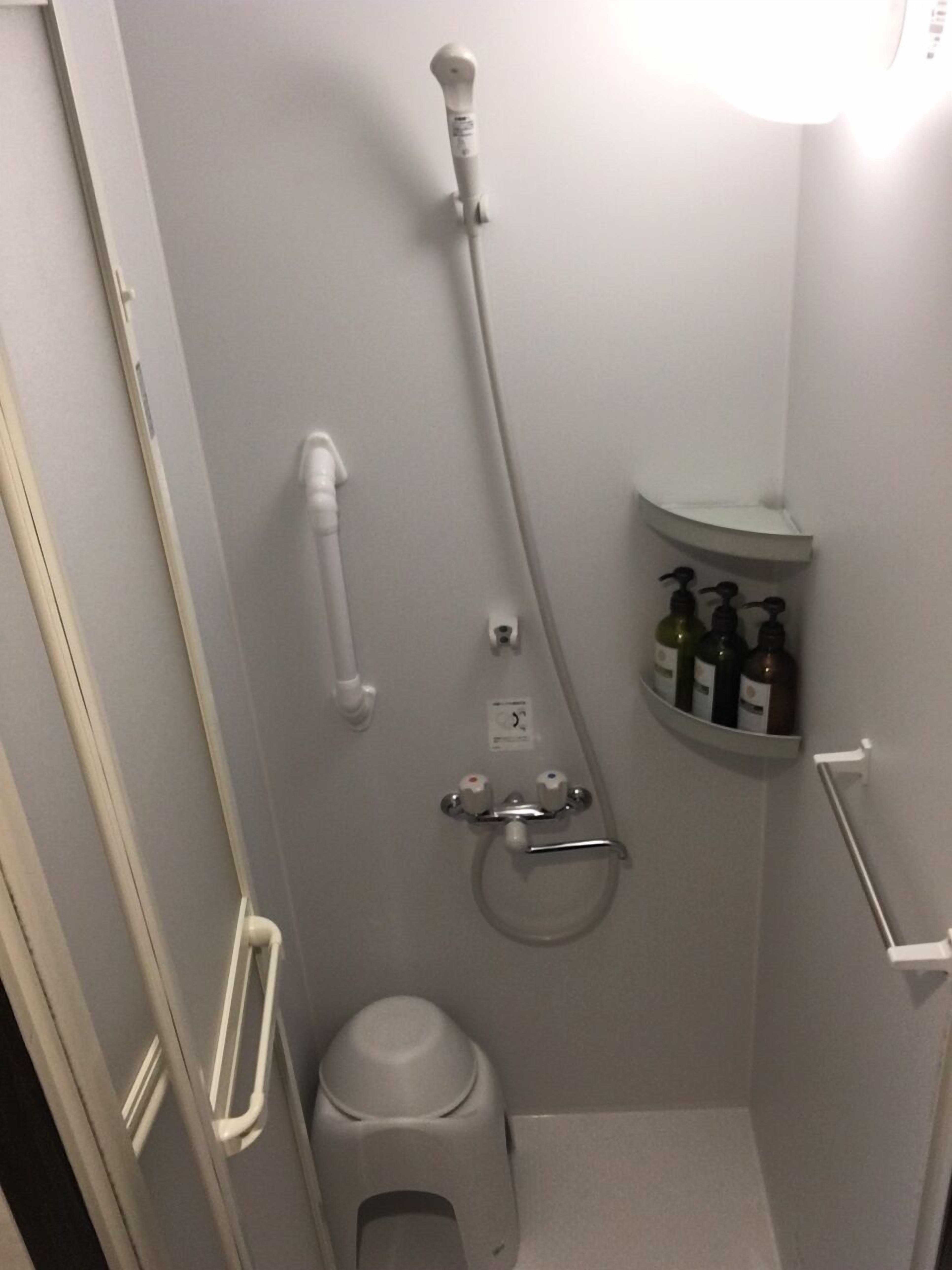 A small, compact bathroom with a shower, toilet, and a shelf with toiletries.