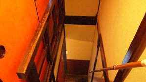 A wooden staircase with a handrail, leading to a landing with a white wall and a black beam. - Korakuan (Kyoto)