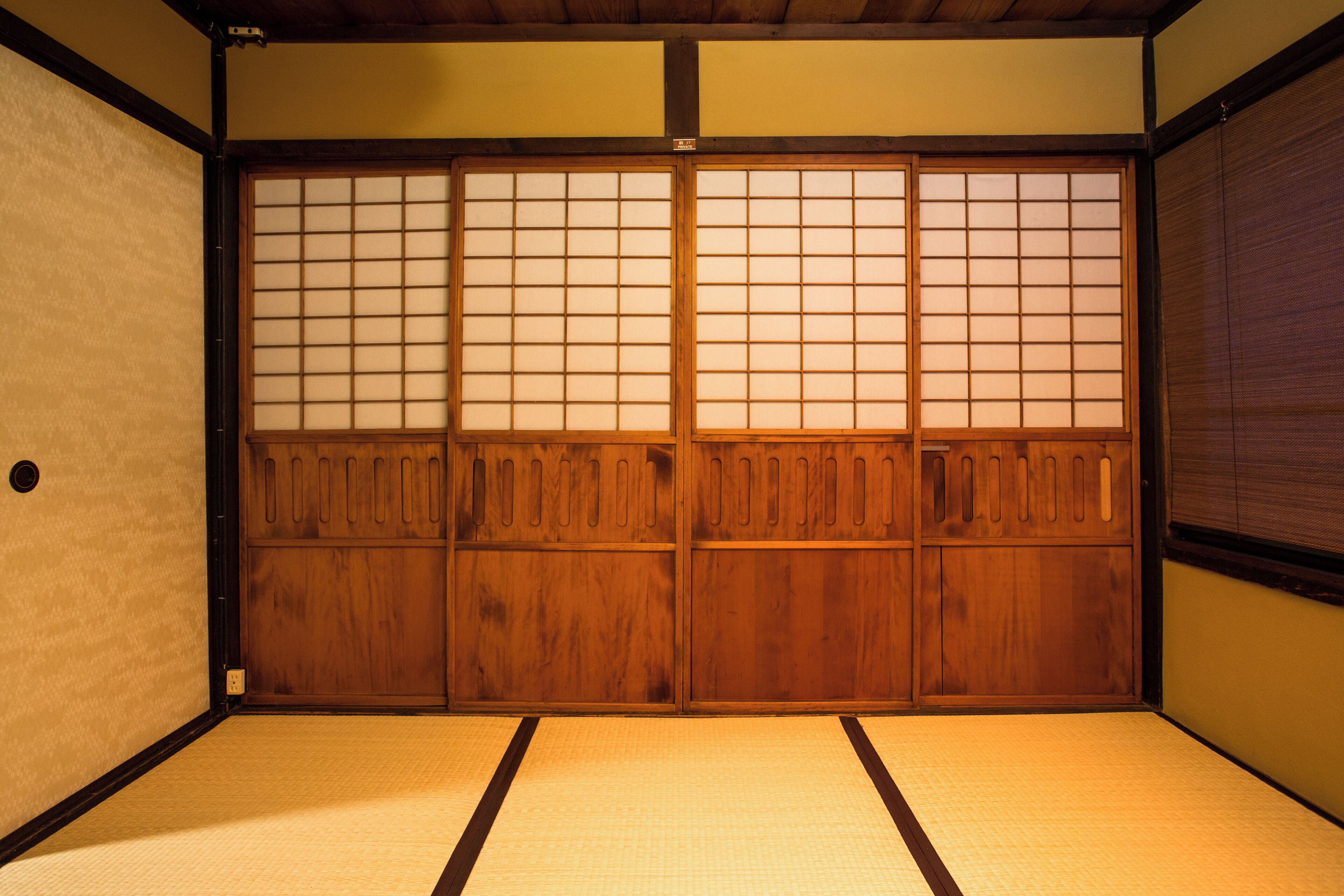 A traditional Japanese room with tatami flooring, sliding shoji doors, and a wooden door.