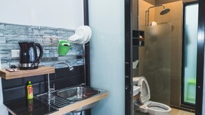 Cocina compacta con microondas, hervidor de agua y escurreplatos. Se observa un cubo pequeño de basura.