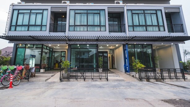Un edificio moderno de dos pisos con un acceso cubierto, ventanas amplias y mesas al aire libre.