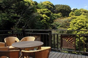 A wooden deck with wicker furniture and a view of dense trees. - Guest House KODOKODO (Minamiizu)
