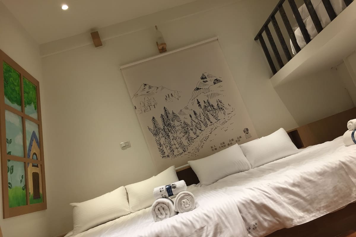 A hotel room with a neatly made bed, a large wall mural, and a wooden floor.