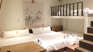 Habitación de hotel con cama, mesa de madera, literas con toallas y un cuadro de un paisaje montañoso en la pared.