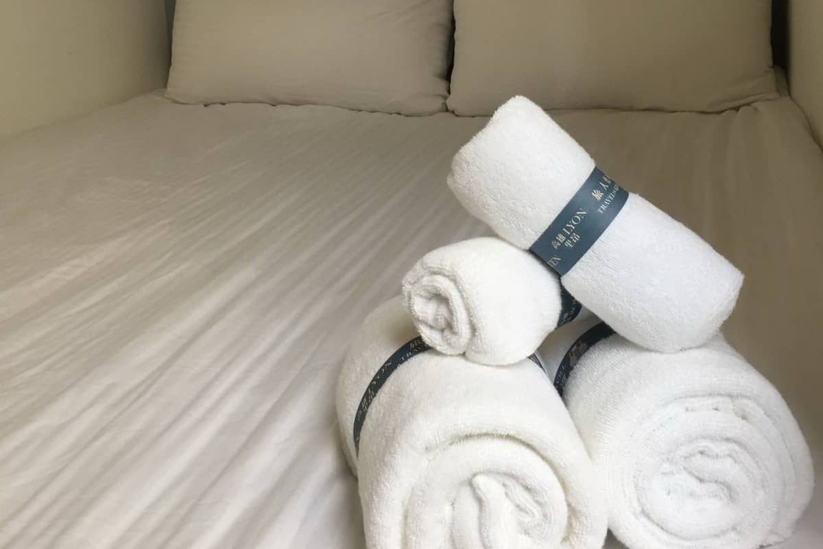 A neatly made bed with beige bedding and pillows, and a stack of white towels with a label on them.