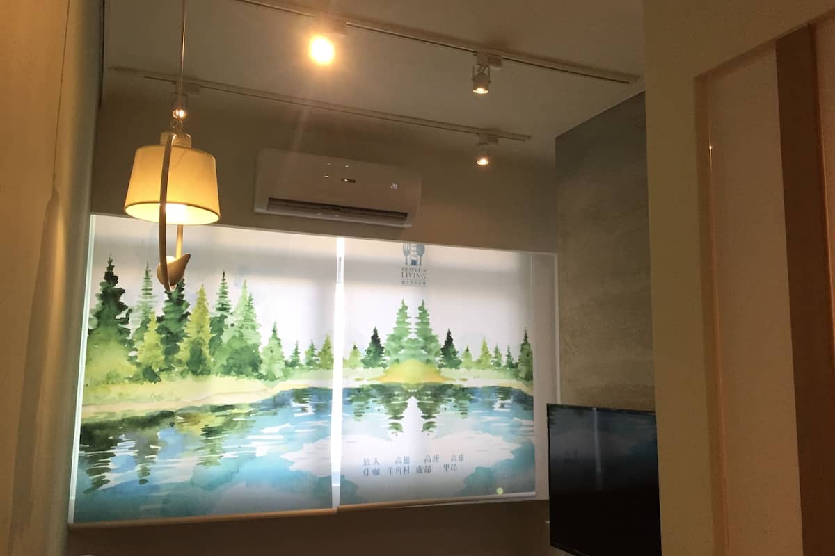 A room with a large wall-mounted artwork depicting a serene landscape with trees and water. There is a ceiling light fixture and an air conditioning unit visible.