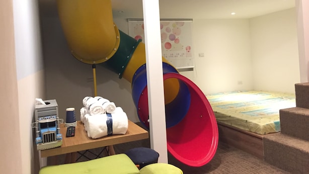 Zona de juegos infantiles con un tobogán, una estructura de juego y una mesa con toallas y juguetes.