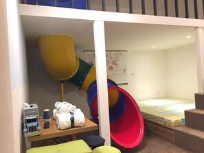 A children's play area with a slide, a play structure, and a table with towels and toys. - Gathering (Kaohsiung)