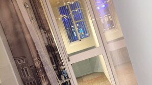 Un baño con ducha, puerta de vidrio y vista a la ciudad iluminada de noche.