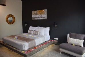 A bedroom with a bed, a chair, a painting, and a wall-mounted lamp. - Pipe Dream Villas Resort (Kuta)