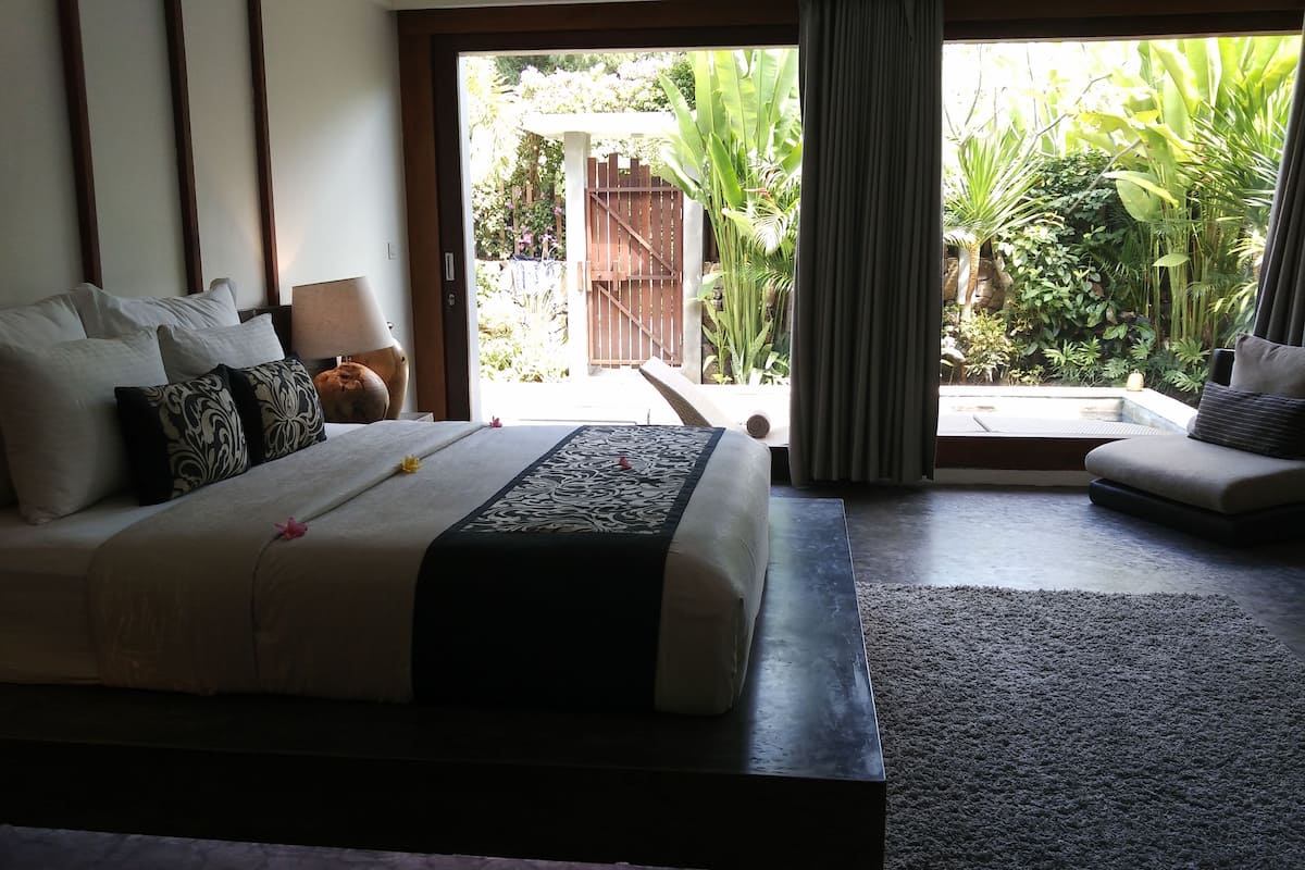 A bedroom with a large bed, a sofa, and a view of a garden through a sliding door.