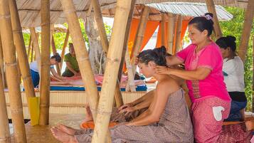 A group of people sitting on mats under a bamboo structure, possibly in a communal area.