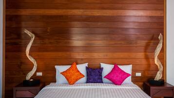 Una cama con una colcha a rayas, tres almohadas con diseños florales y dos esculturas de madera a cada lado.