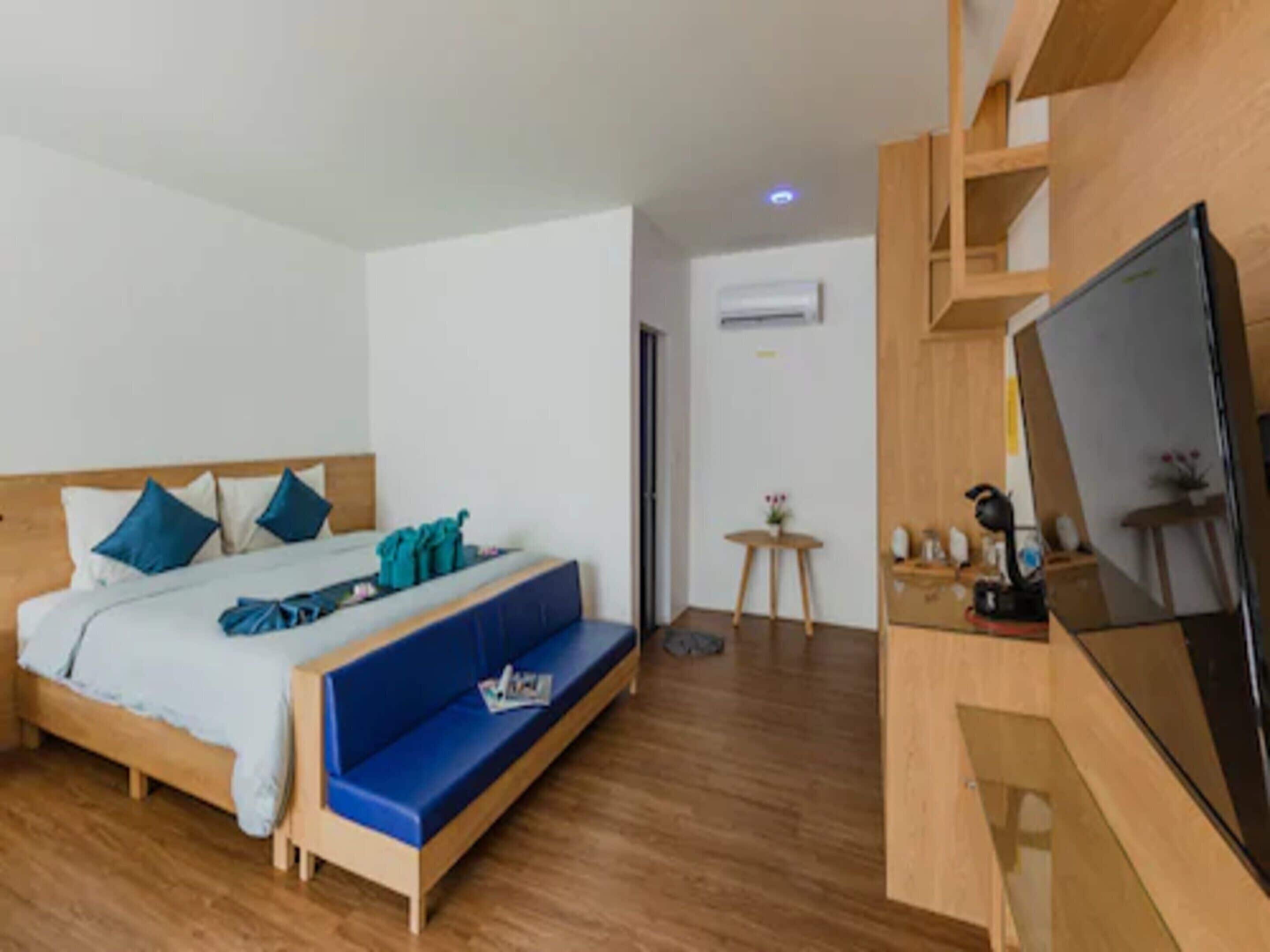 A hotel room with a bed, a blue sofa, a TV, and a small table with a plant.