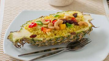 A pineapple filled with yellow rice, red bell peppers, cashews, and raisins on a white plate.