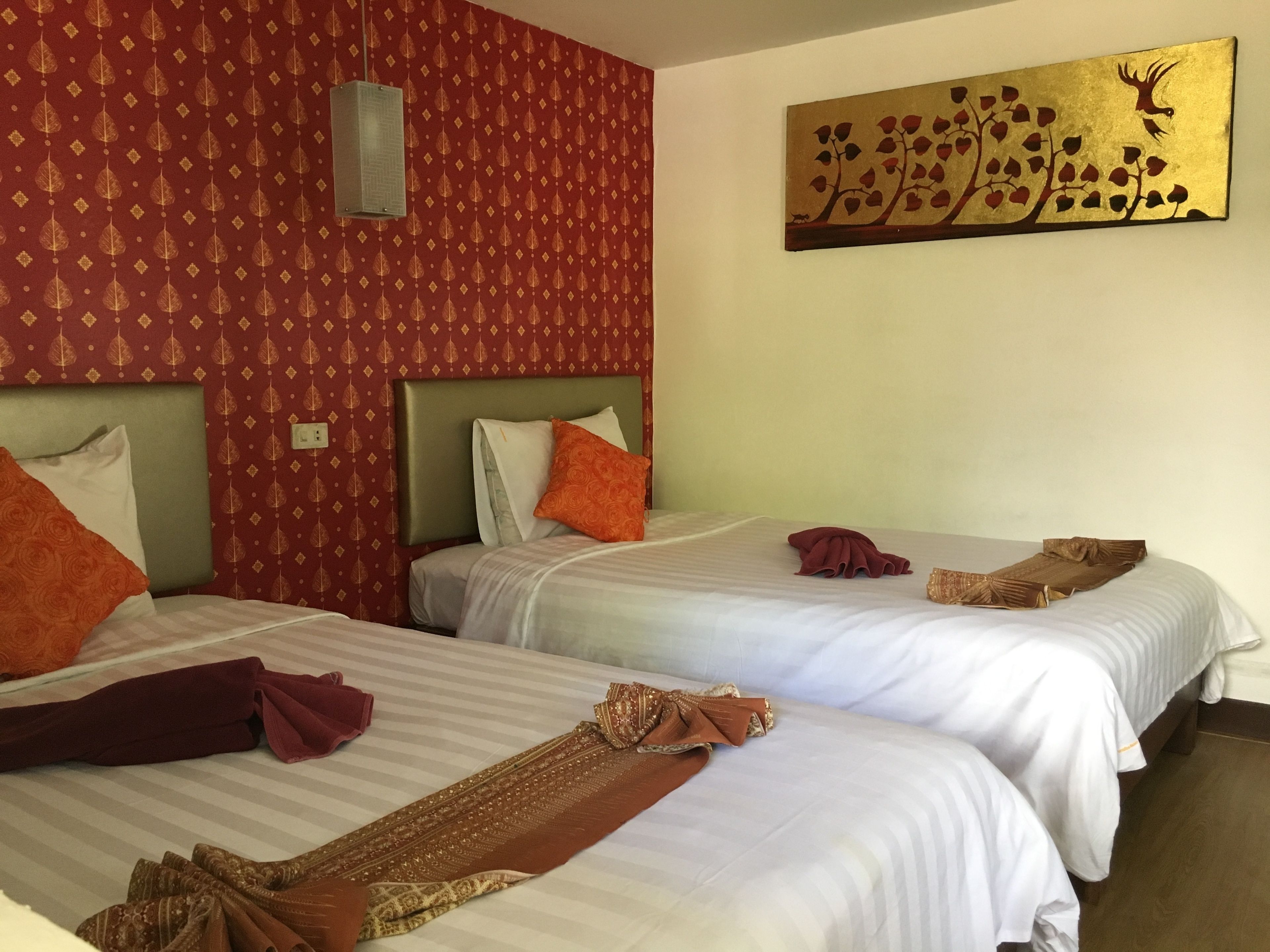 Een hotelkamer met twee bedden, elk voorzien van witte lakens en oranje kussens. Aan de muur hangt een kunstwerk dat een boom met bladeren en een herten toont.