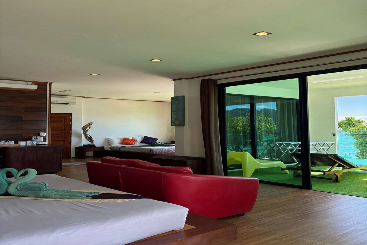 Une chambre d’hôtel moderne avec un lit, un canapé rouge et une vue sur une piscine et un espace verdoyant.