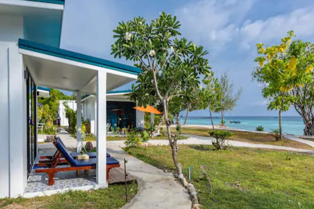 Un bâtiment moderne doté d’un espace extérieur couvert avec des sièges, d’un sentier menant à la plage et offrant une vue sur l’océan.