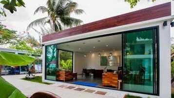 Un edificio moderno con amplios ventanales de vidrio, mobiliario de madera y un entorno de jardín tropical.