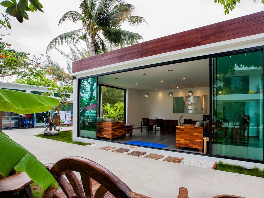Un edificio moderno con amplios ventanales de vidrio, mobiliario de madera y un entorno de jardín tropical.