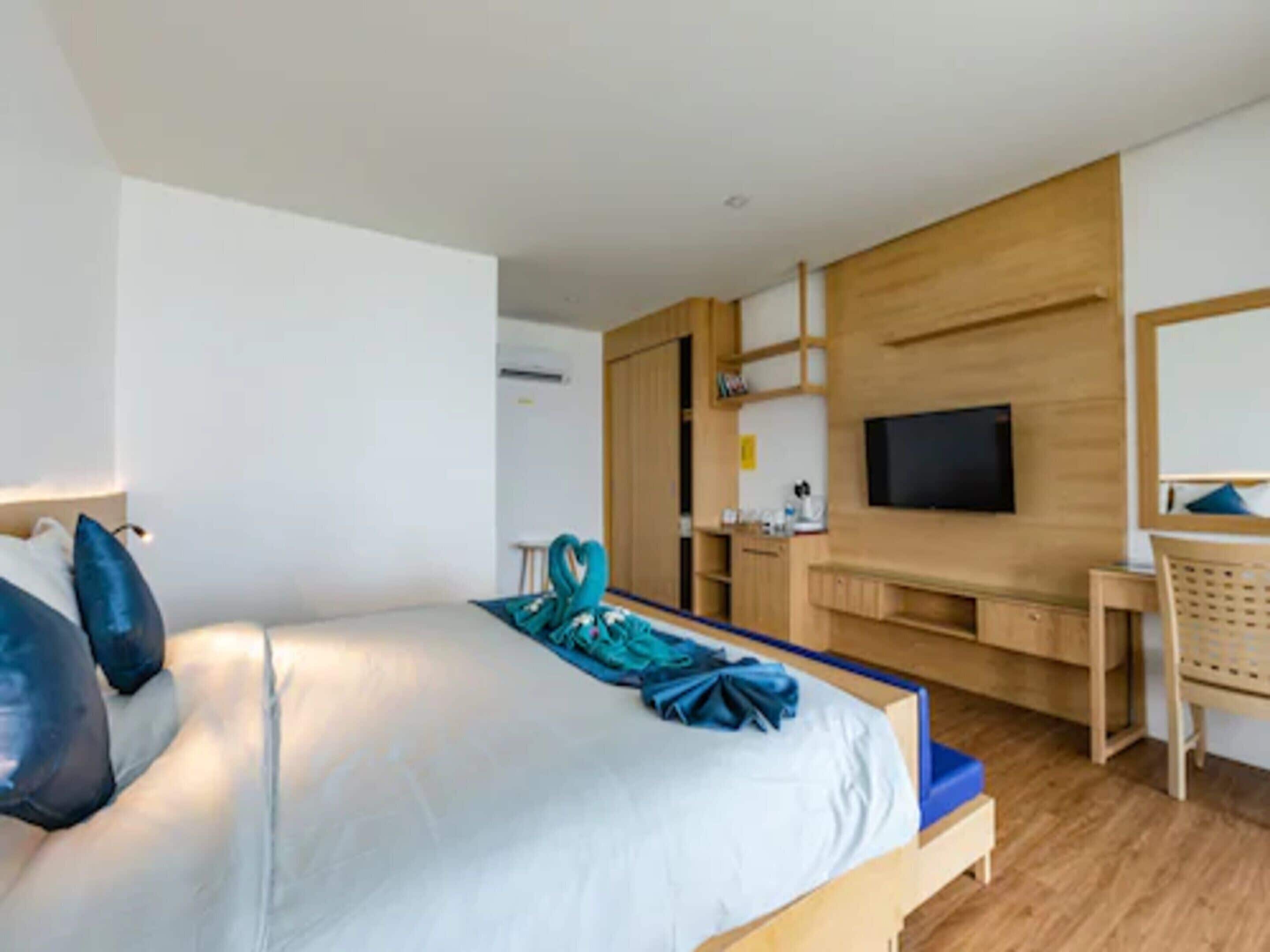 A modern hotel room with a large bed, a desk, a TV, and a wooden wardrobe.