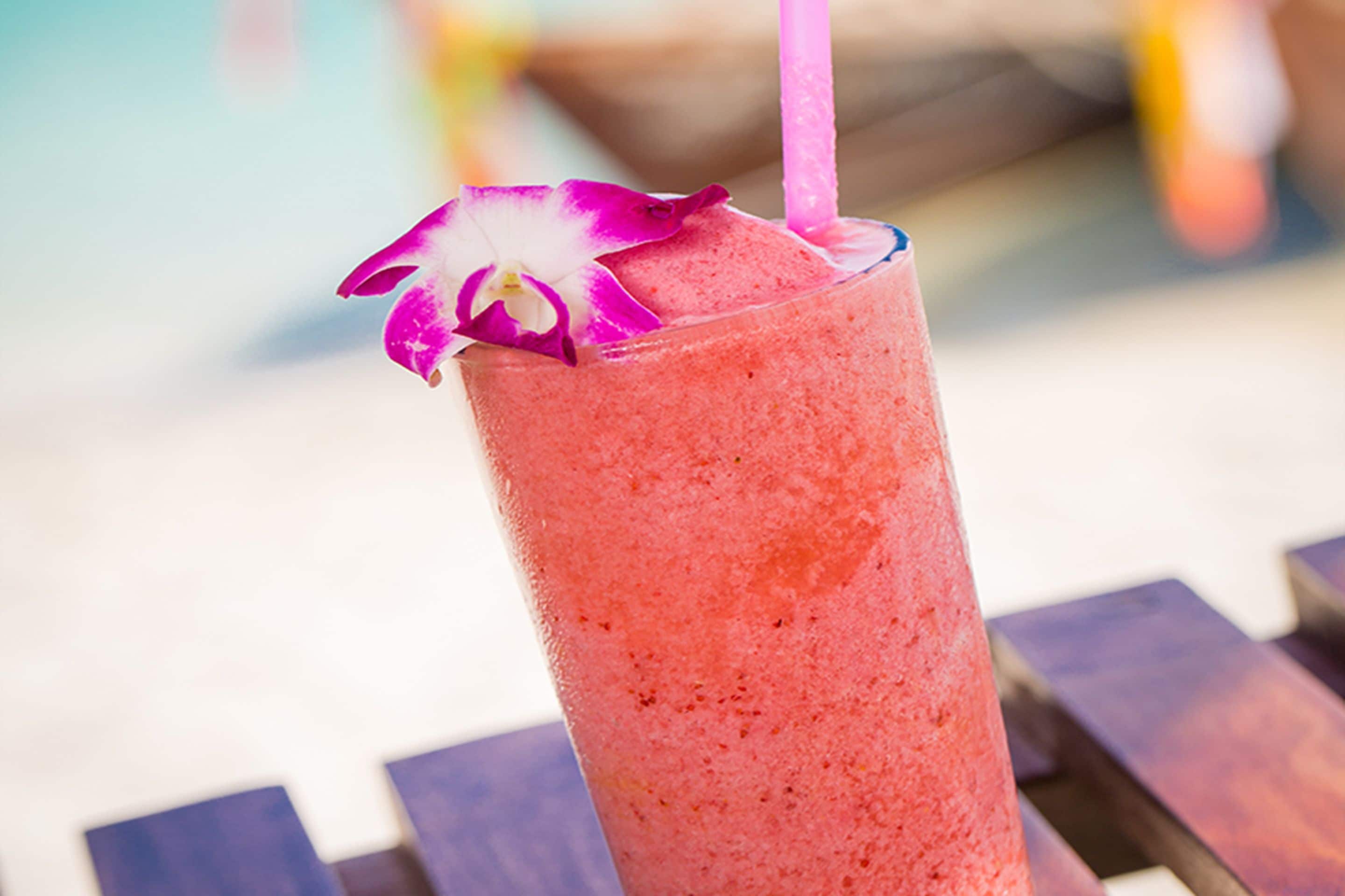A tall glass with a pink beverage, a purple straw, and a purple flower garnish.