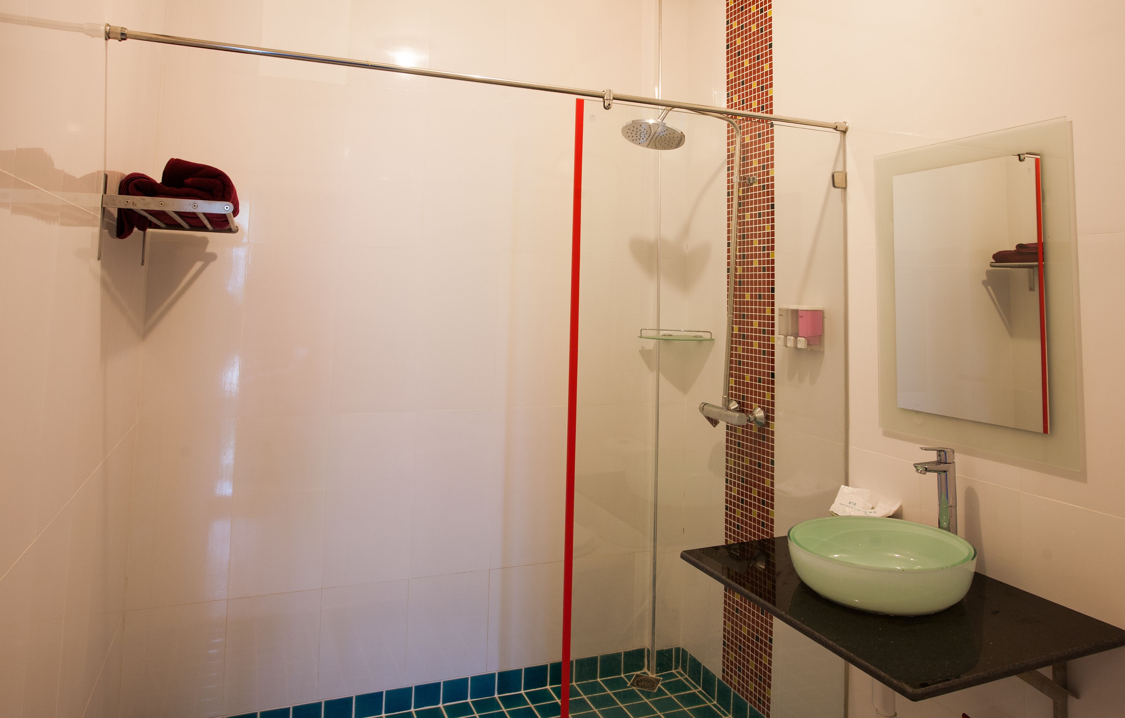 Baño con cabina de ducha de vidrio, lavamanos de vidrio y un espejo.