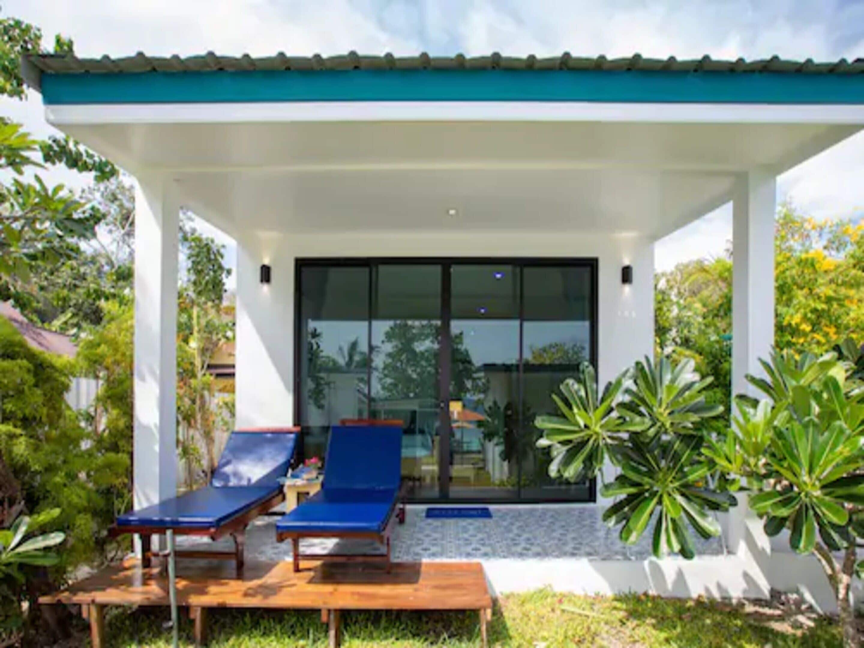 Une maison moderne dotée d’un patio couvert, de deux fauteuils de relaxation et d’une porte vitrée donnant accès à un espace piscine.
