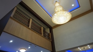 A chandelier with a blue-lit ceiling, wooden paneling, and a balcony with ornate railings.