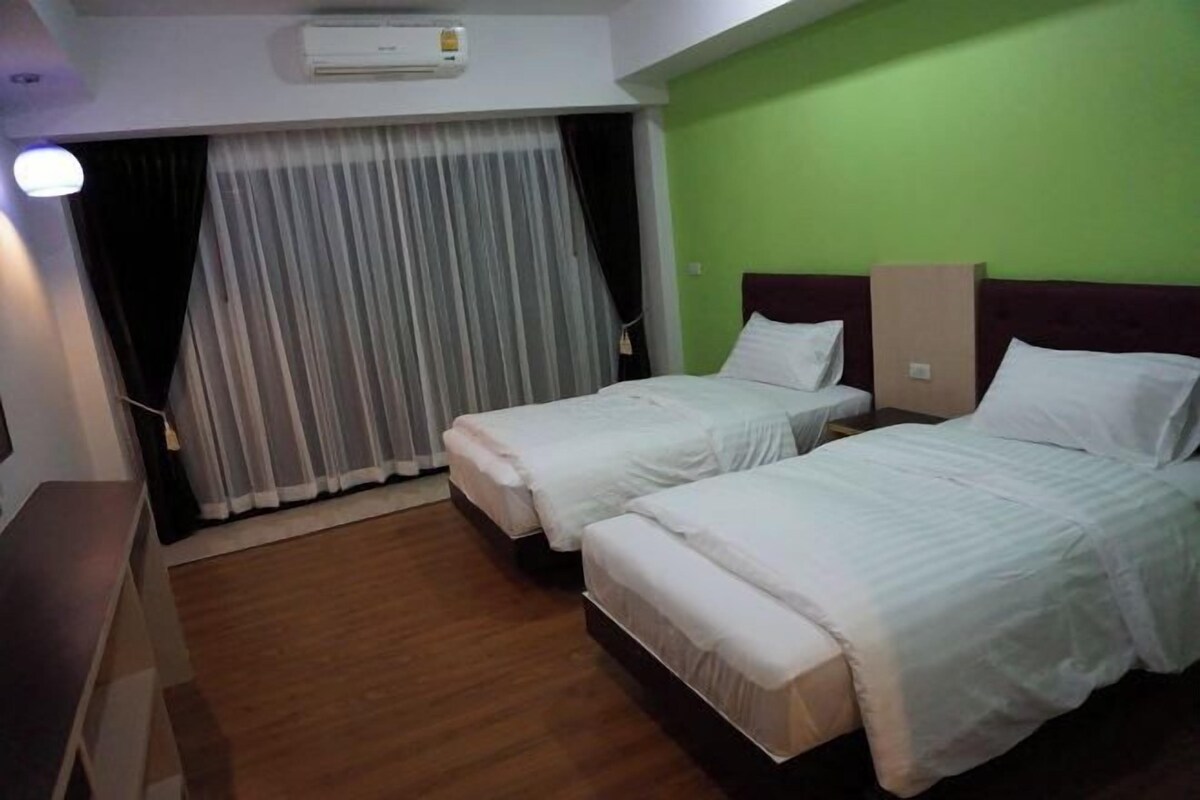 Ein Hotelzimmer mit zwei Einzelbetten, Holzboden, grüner Wand und einem Fenster mit Vorhängen.