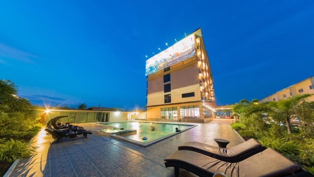 A hotel with a swimming pool, outdoor seating, and a large illuminated sign.