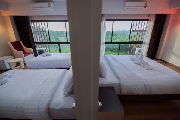 A hotel room with two beds, a chair, and a view of greenery. - Phatra Boutique Hotel (Udon Thani)