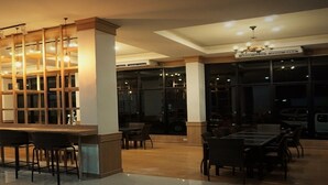 A modern bar area with a long counter, multiple seating options, and a large window providing a view of the outside.