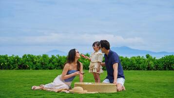 Un pique-nique en famille dans un champ verdoyant, sous un ciel dégagé, avec des montagnes qui se dessinent à l’horizon.