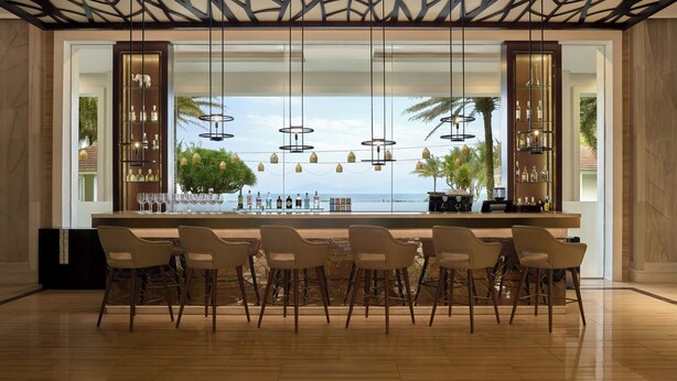A modern bar area with a long counter, multiple bar stools, and pendant lighting. - Renaissance Danang Hoi An Resort & Spa (Da Nang)
