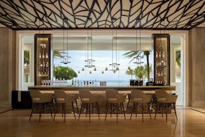 A modern bar area with a long counter, multiple bar stools, and pendant lighting. - Renaissance Danang Hoi An Resort & Spa (Da Nang)