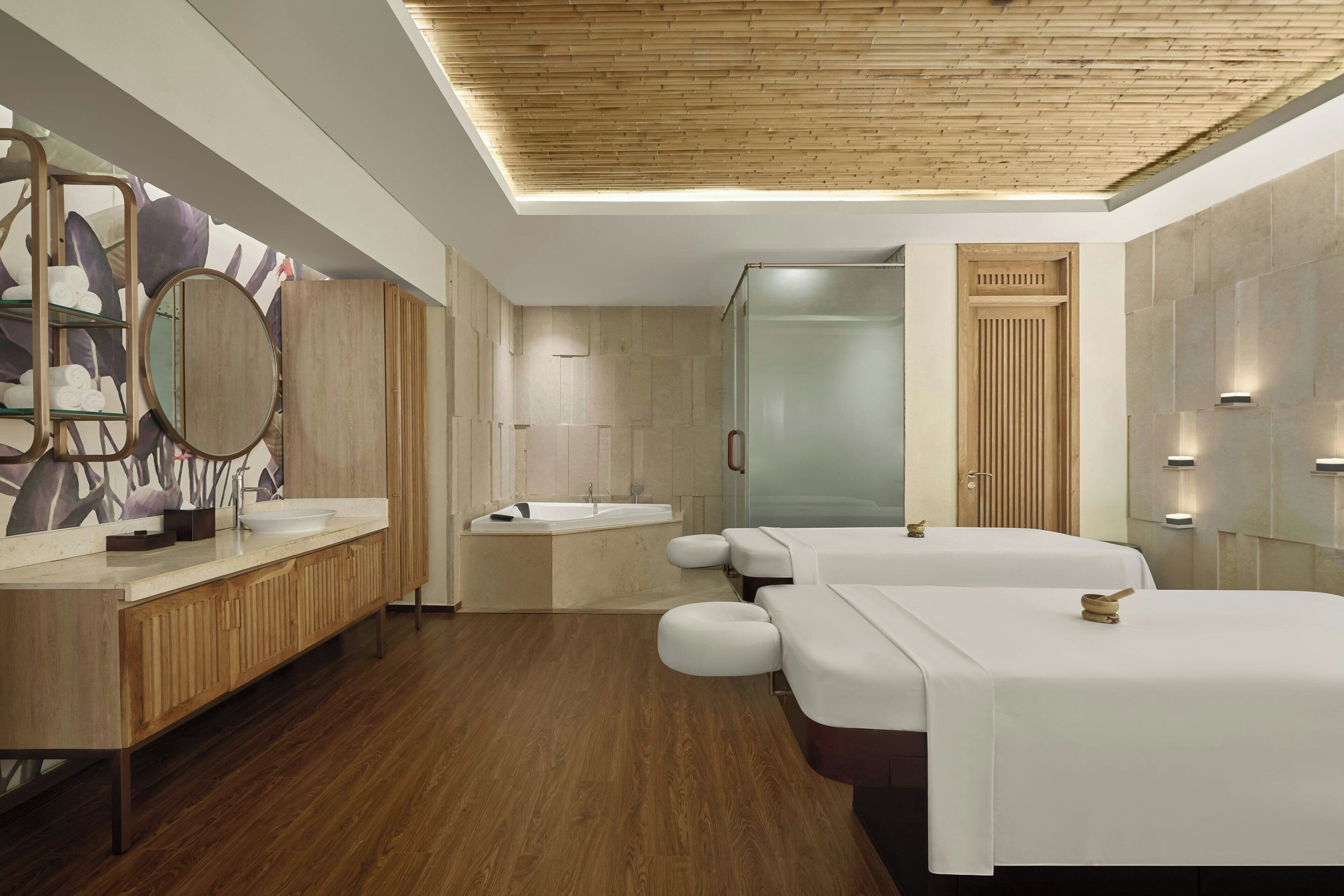 Un baño moderno con suelo de madera, un espejo grande, una bañera y dos camillas de masaje.