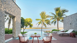 A poolside area with stone walls, two lounge chairs, a small table, and a view of the beach and ocean. - Renaissance Danang Hoi An Resort & Spa (Da Nang)