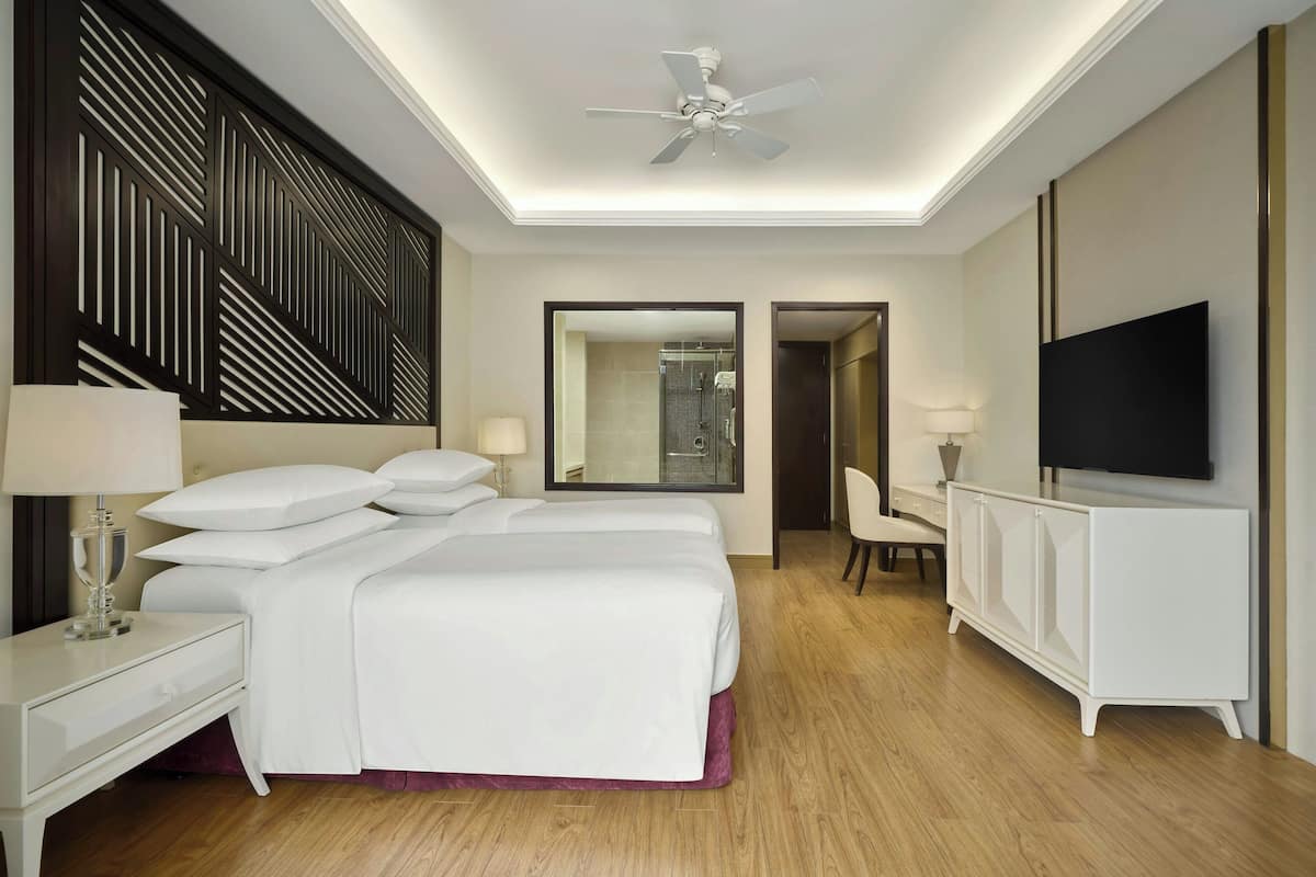 A hotel room with a large bed, a TV, a desk, and a mirror.