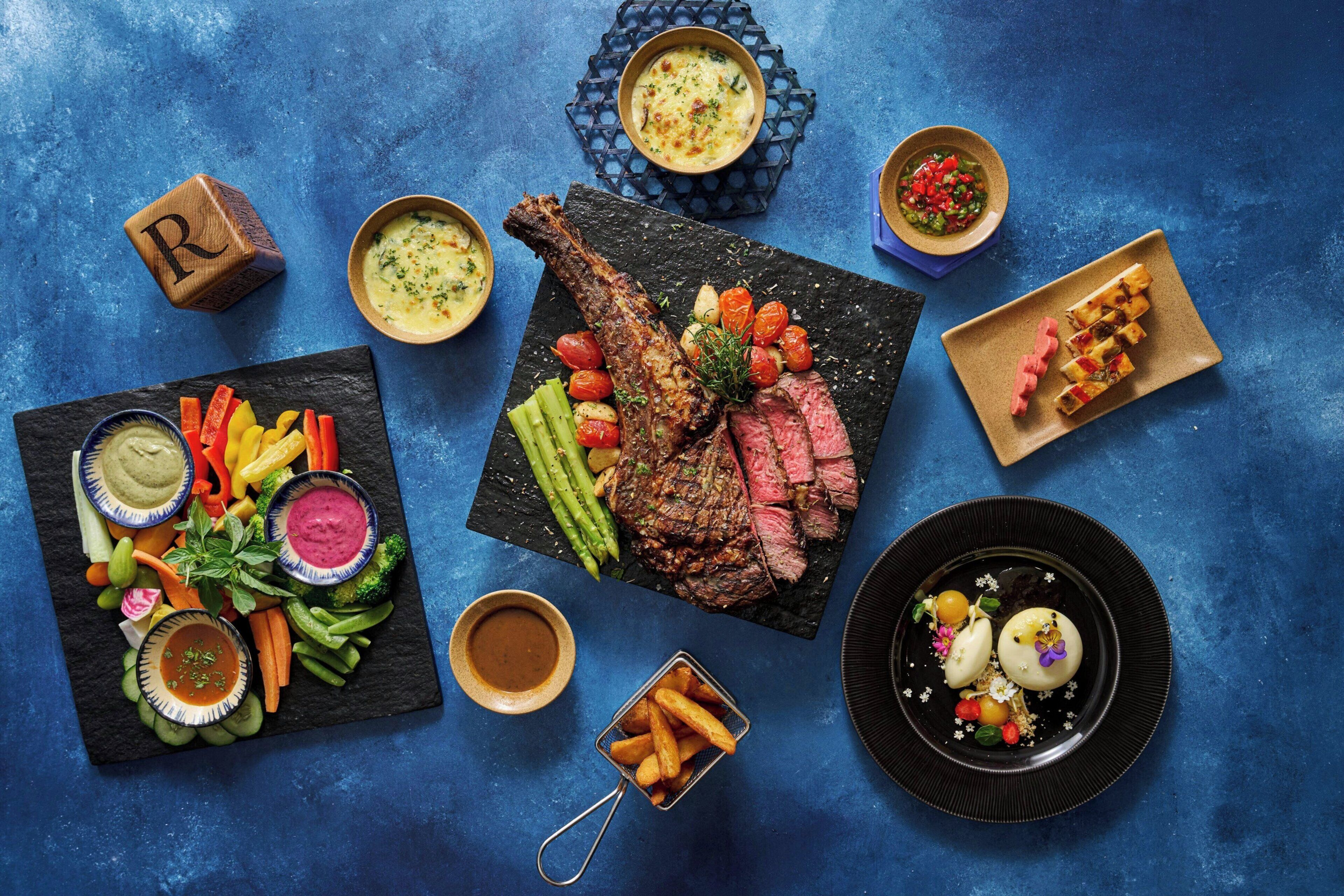 Diversos platos, entre ellos carne, verduras y salsas, sobre un fondo azul.
