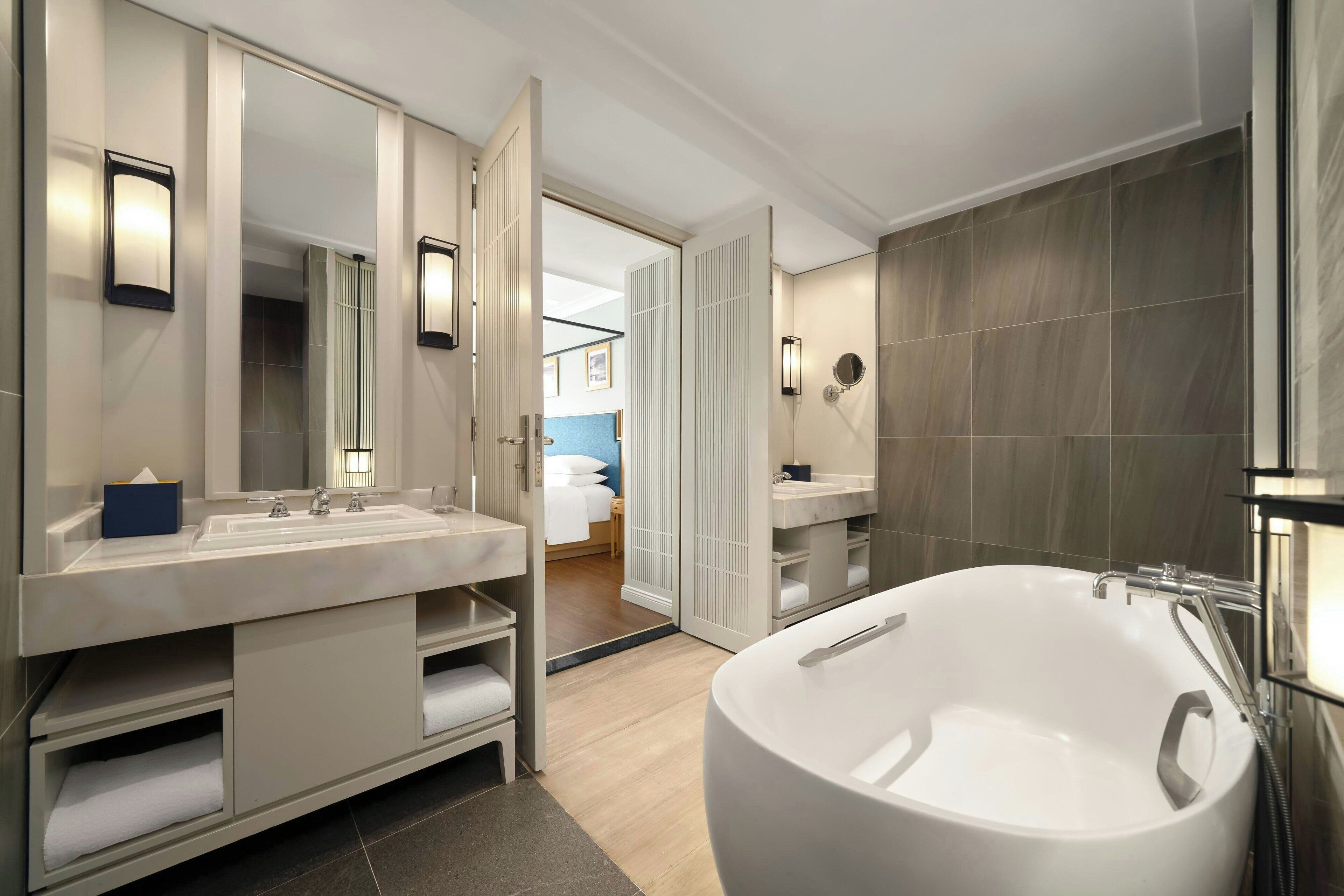 Ein modernes Badezimmer mit einer großen Badewanne, einem Waschtisch inklusive Spiegel und einem separaten Waschbecken.