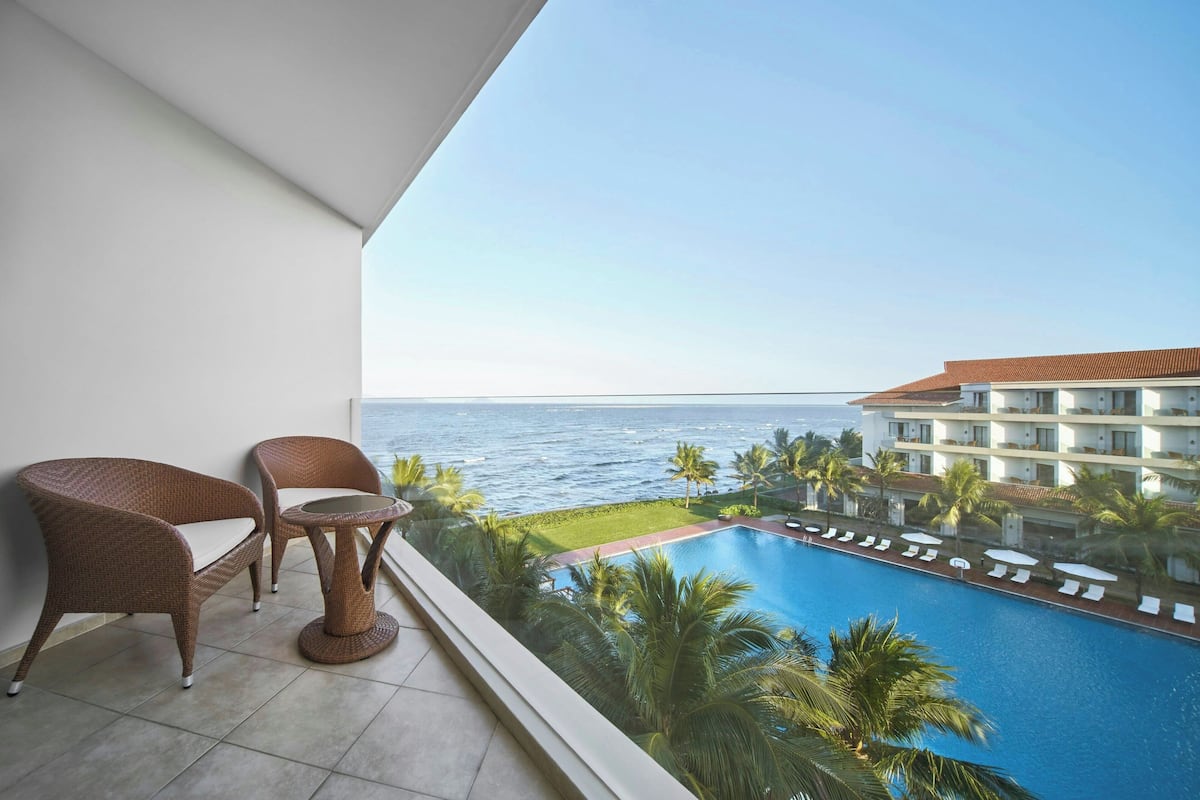 Balcón con mobiliario de mimbre con vista a una piscina y al océano.