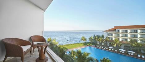 A balcony with wicker furniture overlooking a pool and ocean view.