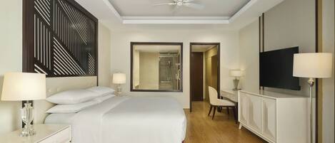 A hotel room with a large bed, a desk, a television, and a ceiling fan.