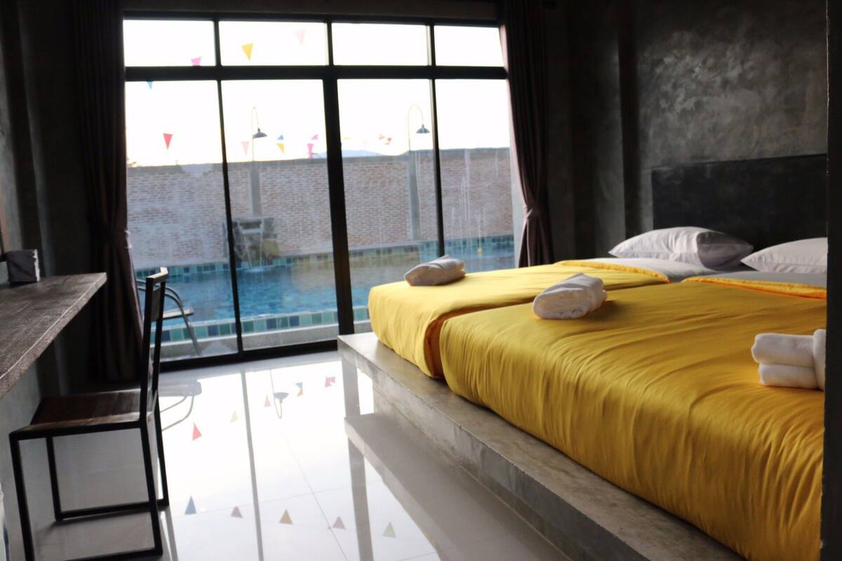 Een hotelkamer met een groot bed, een bureau en uitzicht op een zwembad door een groot raam.